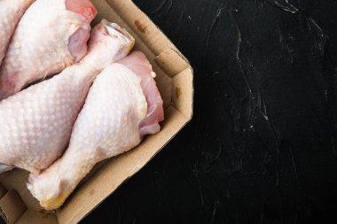 Çiğ tavuk derisi ya da bacak seti, kağıt pakette, siyah taş zemin üzerinde, üst görünüm düz, metin alanı için kopyalama alanı ile