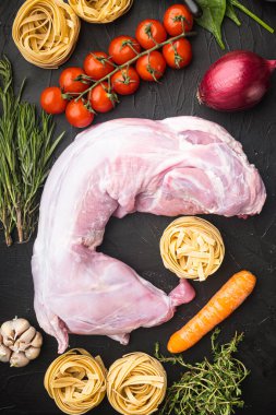 Tam tavşan, baharat ve sebzeli çiğ et, güveç seti malzemeleri, siyah taş arka planda, üst manzara düz.
