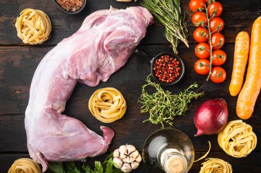 Taze et. Bütün tavşan yahni pişirmeye hazır. Tagliatelle seti, eski, siyah ahşap masa arkaplanı, üst manzara düz.