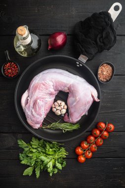 Tüm çiğ tavşan malzeme seti, dökme demir kızartma tava, siyah ahşap masa arka planı, üst görünüm düz yatıyordu