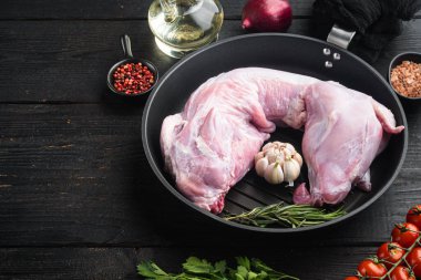 Çiğ ve taze et. Tüm tavşan malzemelerle pişirmeye hazır, dökme demir kızartma tavasında, siyah ahşap masa zemininde, metin için fotokopi alanı ile