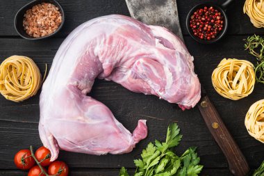 Çiğ tavşan eti ve pişirme malzemeleri güveç tagliatelle seti, siyah ahşap masa arka planı, üst görünüm düz yatıyordu