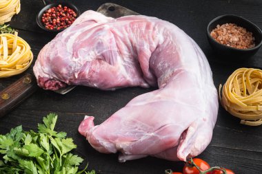 Tam tavşan, baharat ve sebzeli çiğ et, güveç seti malzemeleri, siyah ahşap masa arkaplanı.