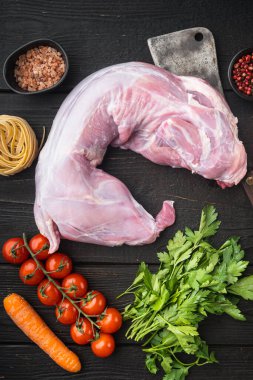 Çiğ tavşan eti ve taze sebzeler yemek için hazır, siyah ahşap masa arkasında, üst manzara düz yatıyordu.