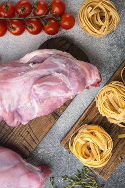 Çiğ tavşan eti ve yemek malzemeleri güveç tagliatelle seti, gri taş arka planda, üst görünüm düz yatıyordu