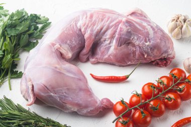 Çiğ ve taze et. Beyaz taş arka planda, malzemelerle pişirmeye hazır bir tavşan.