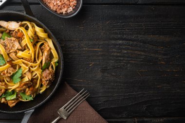 Chanterelleli Tagliatelle ve pişirilmiş tavşan seti, kızgın demir tavada veya tencerede, siyah ahşap masa üzerinde, üst görünüm düz, metin için yer