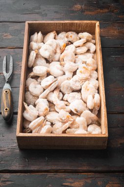 Buzlu pembe donmuş karidesler. Pişmemiş kabuklu deniz ürünleri seti, ahşap kutuda, eski, siyah ahşap masada.