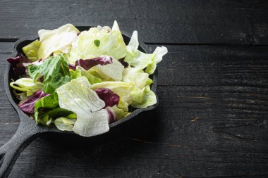 Salata yaprakları seti, dökme demir tavada veya tencerede, siyah ahşap masa üzerinde, metin için kopyalama alanı ile
