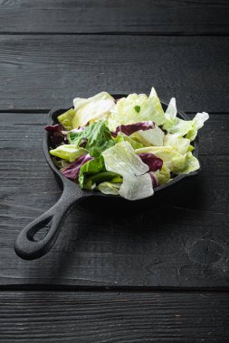 Ispanaklı taze yeşil salata, romaine ve marul seti, kızgın demir tavada veya tencerede, siyah ahşap masa üzerinde