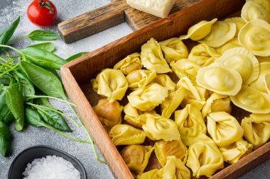 Taze malzemeli İtalyan çiğ Ravioli, fesleğen, pesto, jambon, mozzarella peyniri, parmesan seti, ahşap kutuda, gri arka planda.