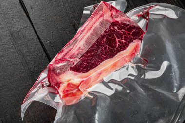 Taze, büyük ve iştah açıcı kulüp bifteği vakum paketleme seti, siyah ahşap masa arka planında
