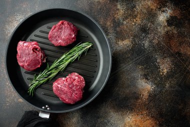 Baharatlı çiğ sığır fileto bifteği ve tüm mermer fileto kesim seti, dökme demir kızartma tavasında, eski koyu kırsal arka planda, üst görünüm düz, metin için kopya alanı ile