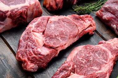 Çiğ mermer biftek seti, pirzola kesimi, eski siyah ahşap masa arka planında.