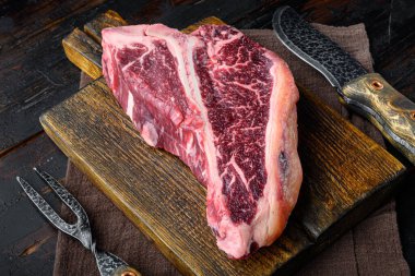 Kuru yaşlı Raw T-bone veya biftek mermer biftek set, ahşap kesim tahtası üzerinde, eski siyah ahşap masa arka planı