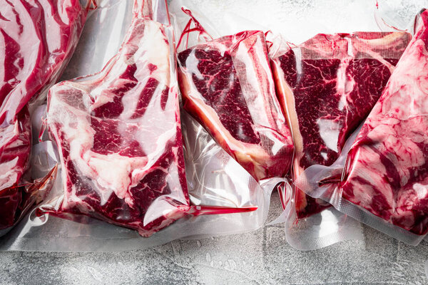 Beef steak vacuum sealed ready for sous vide cooking set, tomahawk, t bone, club steak, rib eye and tenderloin cuts, on gray stone background