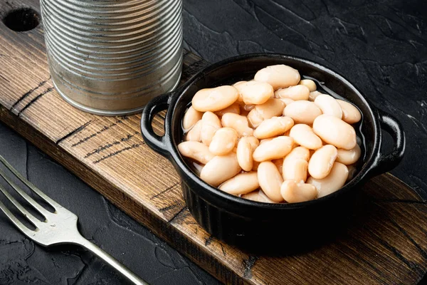 White canned beans set, with metal can, in bowl, on black stone background