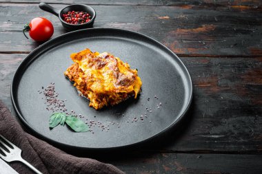 Bechamel peyniri ve Bolonez soslu klasik et lazanyası tabakta, eski, siyah ahşap masa zemininde, metin için fotokopi alanı ile.