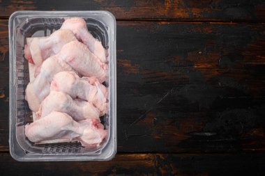 Plastik paket kanatları içinde çiğ tavuk kanatları, eski koyu ahşap masa arkaplanı üzerinde, üst görünüm düz, metin alanı için kopyalama alanı ile