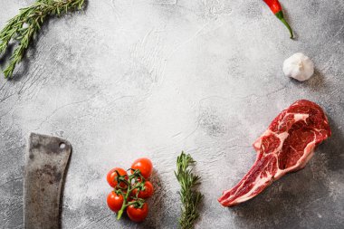 Çiğ siyah angus tomahawk bifteği ya da Amerikan bıçaklı spencer bifteği gri taş masa tahtası üzerinde kesilmiş üst çerçeve, baharatlar, domatesler, sarımsak, biberiye. Metin için boşluk.