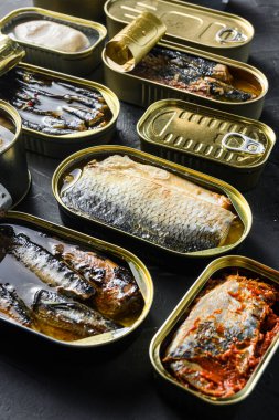 Saury, uskumru, sprat, sardalya, sardalya, kalamar, ton balığı, teneke kutuda konserve balık. Siyah sayfa arkaplan yan görünümü üzerinde aç ve kapat.