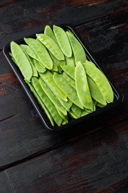 Sağlıklı bezelye seti, plastik kabın içinde, eski siyah ahşap masa arka planında.