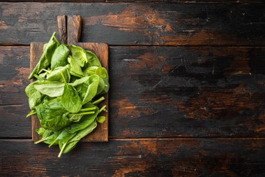 Genç çiğ ıspanak seti, ahşap kesim tahtasında, eski koyu ahşap masa zemininde, üst görünümü düz, metin alanı için fotokopi alanı ile