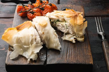 Rus mutfağı doldurulmuş tavuk pirzolası kiev usulü, fırında kiraz domatesli, servis tahtasında, eski, siyah ahşap masa arkasında