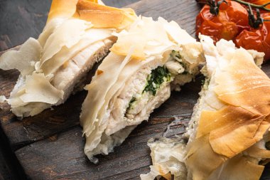 Yabani sarımsaklı tavuk Kiev, fırında kiraz domatesli, servis tahtasında, eski, siyah ahşap masa arkasında