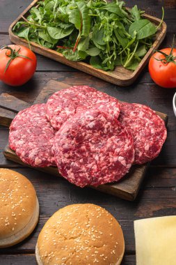 Ev yapımı hamburger. Çiğ et köfteleri, susamlı çörekler ve diğer malzemeler, eski, siyah ahşap masa arka planında.