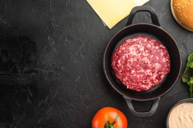 Ev yapımı hamburger. Çiğ et köfteleri, susamlı çörekler ve diğer malzemeler, siyah taş zemin üzerinde, üst görünüm düz, metin alanı için kopyalama alanı