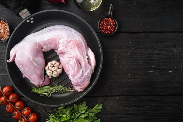 Fresh whole  rabbit meat with with lemon, salt and parsley set, in cast iron frying pan, on black wooden table background, top view flat lay, with copy space for text
