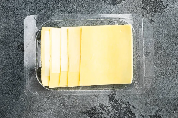 Yellow cheese slices of cheddar set, in plastic pack, on gray stone background, top view flat lay
