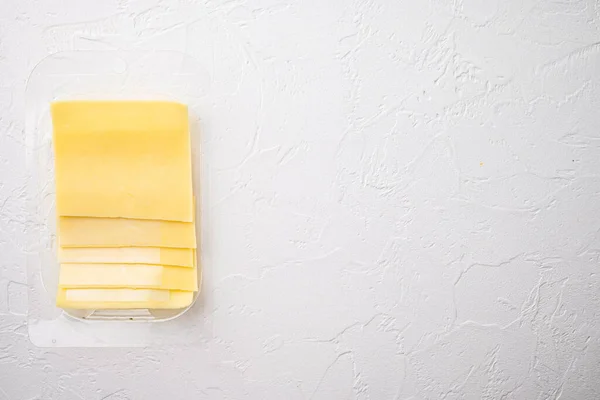 Yellow cheese slices of cheddar set, in plastic pack, on white stone  background, top view flat lay, with copy space for text