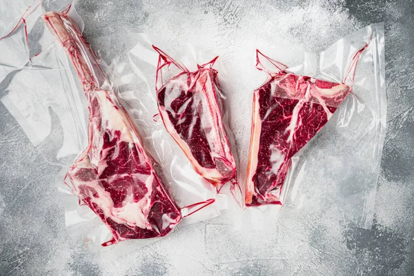 Vakumlanmış çiğ biftek paketlenmiş hava geçirmez sous vide çanta seti, tomahawk, t kemik ve kulüp biftek kesim, gri taş arka planda, üst düz yatıyordu