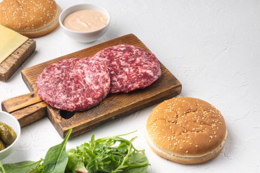 Ev yapımı hamburger. Çiğ et köfteleri, susamlı çörekler ve diğer malzemeler, beyaz taş zemin üzerinde, metin için kopyalama alanı ile