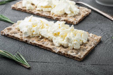 Taze çavdar gevrekleri krem peynir setiyle gri masa arkasında.