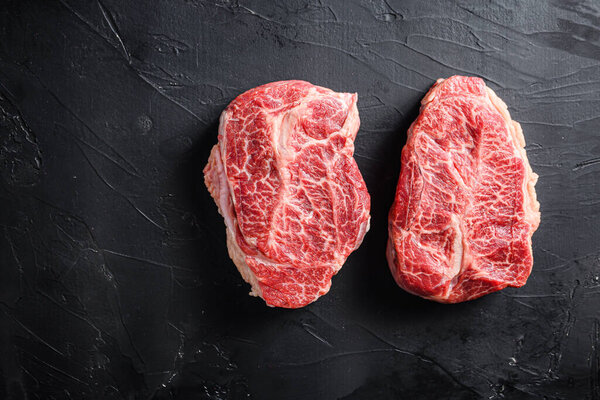 Raw top blade flat Ironcut, on black slate , bio marbled beef  with herbs tomatoes peppercorns overblack stone surface background  top view space for text.