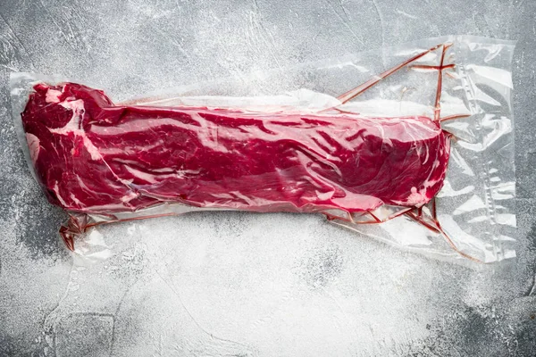 Taze ve çiğ et. Vakumlu plastik market çantasındaki fileto parçasının tamamı gri taştan arka planda, üst görünüm düz yerde, metin alanı için kopyalama alanı var.