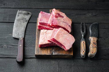 Çiğ organik biftek pirzolası pişmeye hazır, ve eski kasap bıçağı, siyah ahşap masa arkasında.