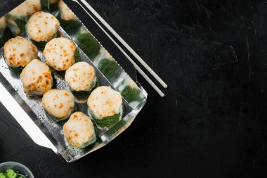 Suşi rulolarını, Philadelphia rulolarını ve fırınlanmış karidesleri alıp siyah taş arka planda, metin için yer ve metin alanlarına koyun.