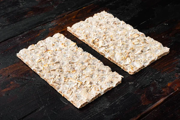 Bir yığın kepekli çıtır ekmek, ayçiçeği, chia ve susam tohumları, eski koyu ahşap masa arka planında.