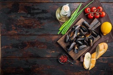 Beyaz şarap setinde haşlanmış midyeler, ahşap kesim tahtasının üzerinde, eski siyah tahta masa zemininde, üst görünüm düz yerde, kopyalanacak yer ve metin için yer var.