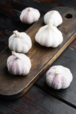 Bir yığın organik çiftlik sarımsağı, ahşap kesim tahtasının üzerinde, eski, siyah ahşap masa arkasında