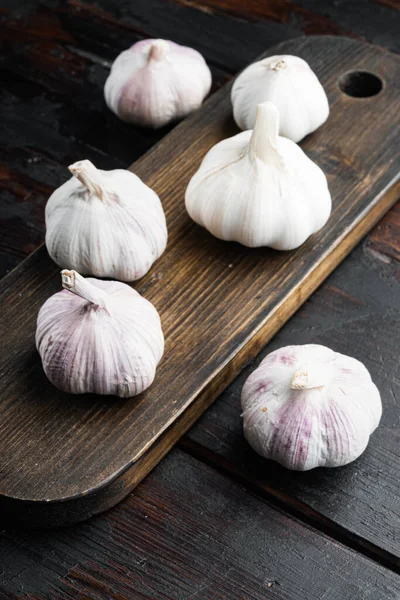 Bir yığın organik çiftlik sarımsağı, ahşap kesim tahtasının üzerinde, eski, siyah ahşap masa arkasında
