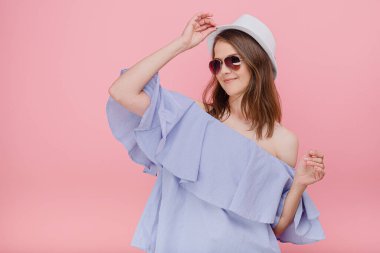 Başarılı bayan öğrenci, kollarını güneş gözlükleriyle açıp şapkasının yakınına dokununca pembe arka plan modeline şaşırıyor.