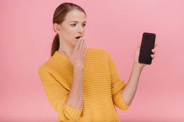 Kadın modelin yatay portresi. Elinde çiziklerle telefonu tut ve ağla. Pembe arka planda üzül.