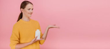 Moda mankeni, boş birine besleyici maddeler sunuyor. Pembe arka planda zevkle bir kenara bakıyor.