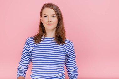 Sevimli bir kadın, mutlu bir ifadeyle pembe arka plan modele olumlu bakıyor.