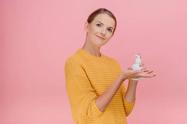 Brunette female use ethyl alcohol hand gel being confident against pink background cleaning concept